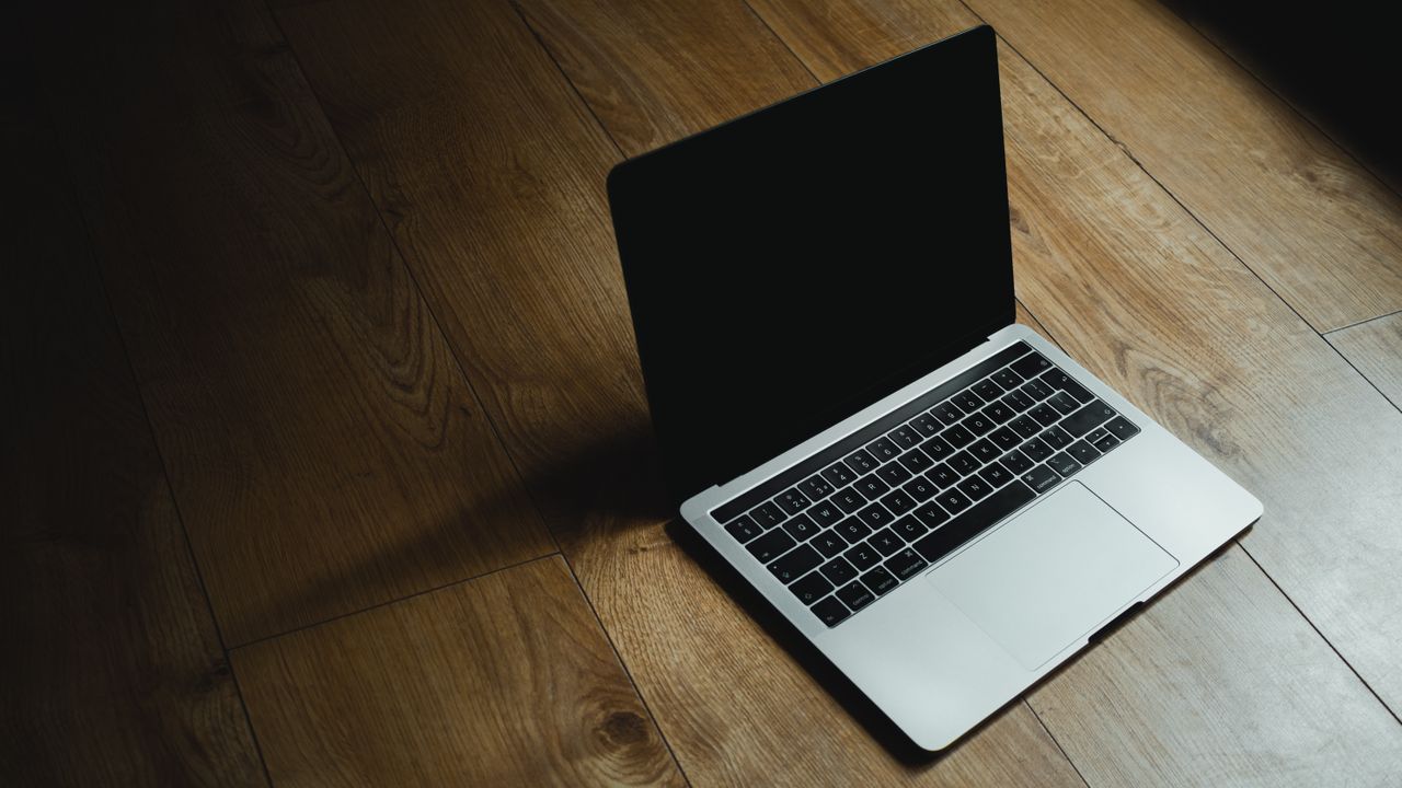 Services MacBook placed diagonally on a warm wooden floor with soft lighting.