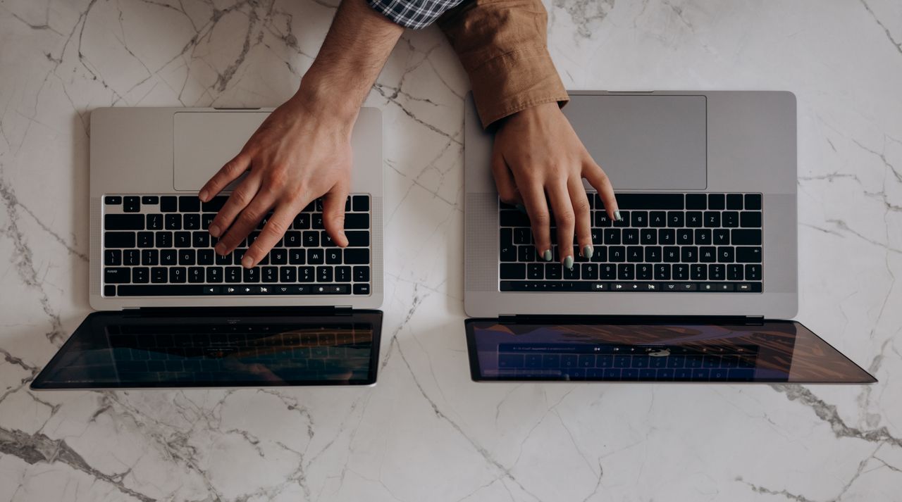 About Two individuals typing on laptops from a top view angle, showcasing collaborative work.